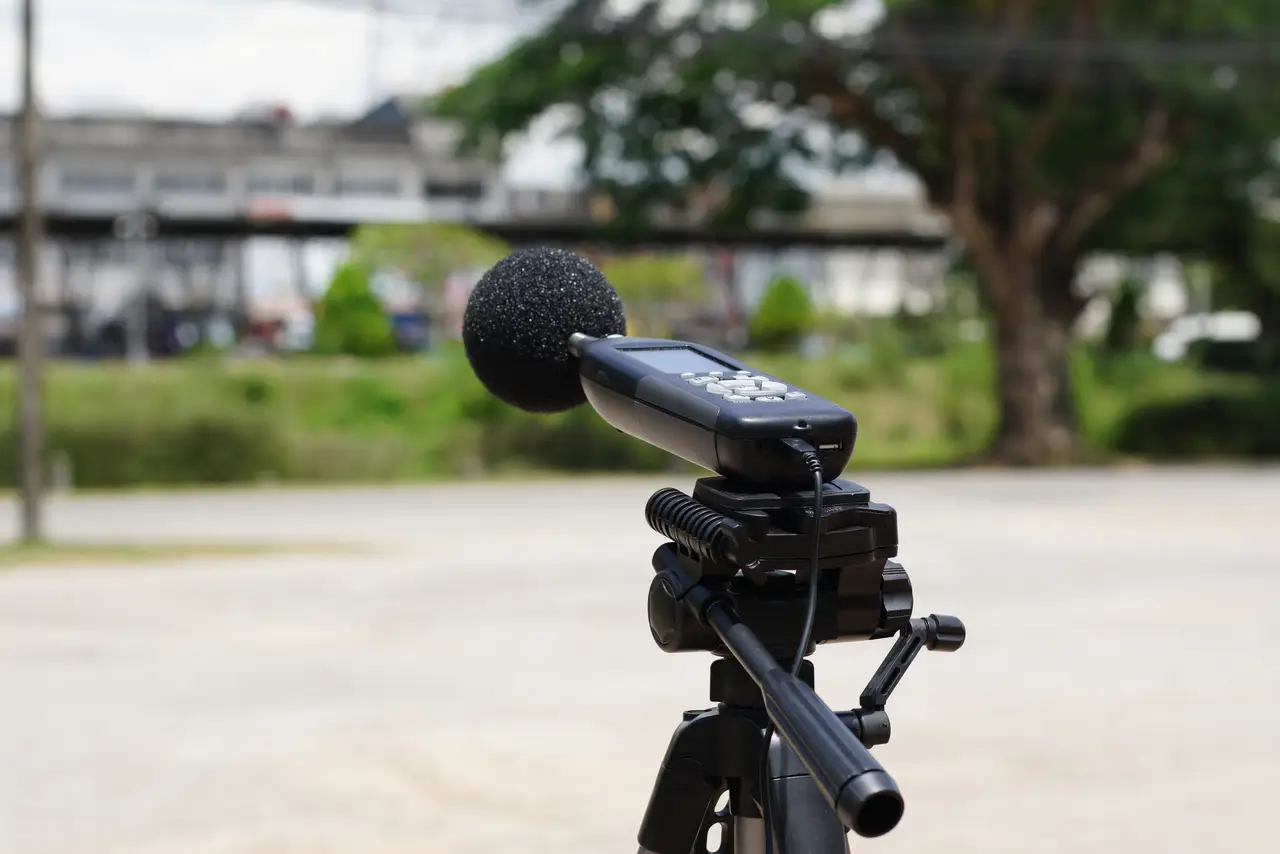 Sound level meter with windscreen on a tripod, recording environmental noise during an acoustic survey